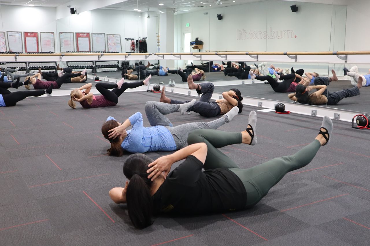 Group of adults participating in a vigorous indoor fitness class focused on core strength exercises.