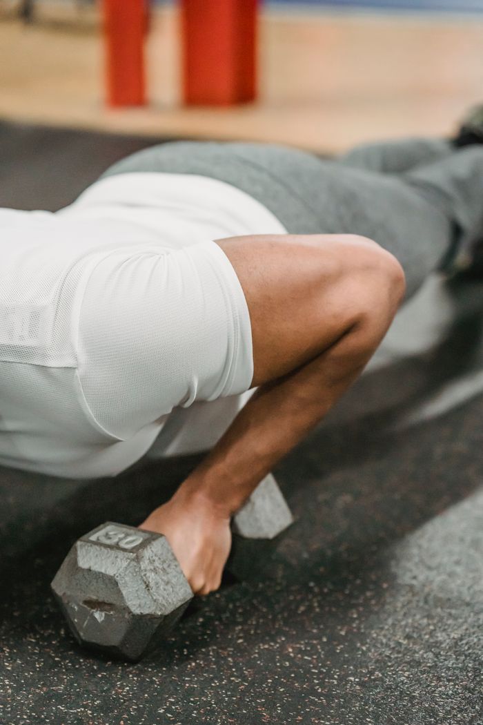 Crop unrecognizable male athlete in sportswear performing push up with dumbbells during workout in gym